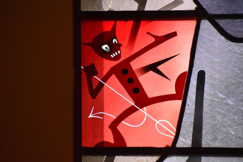 stained glass window image of a little red devil with a pitchfork