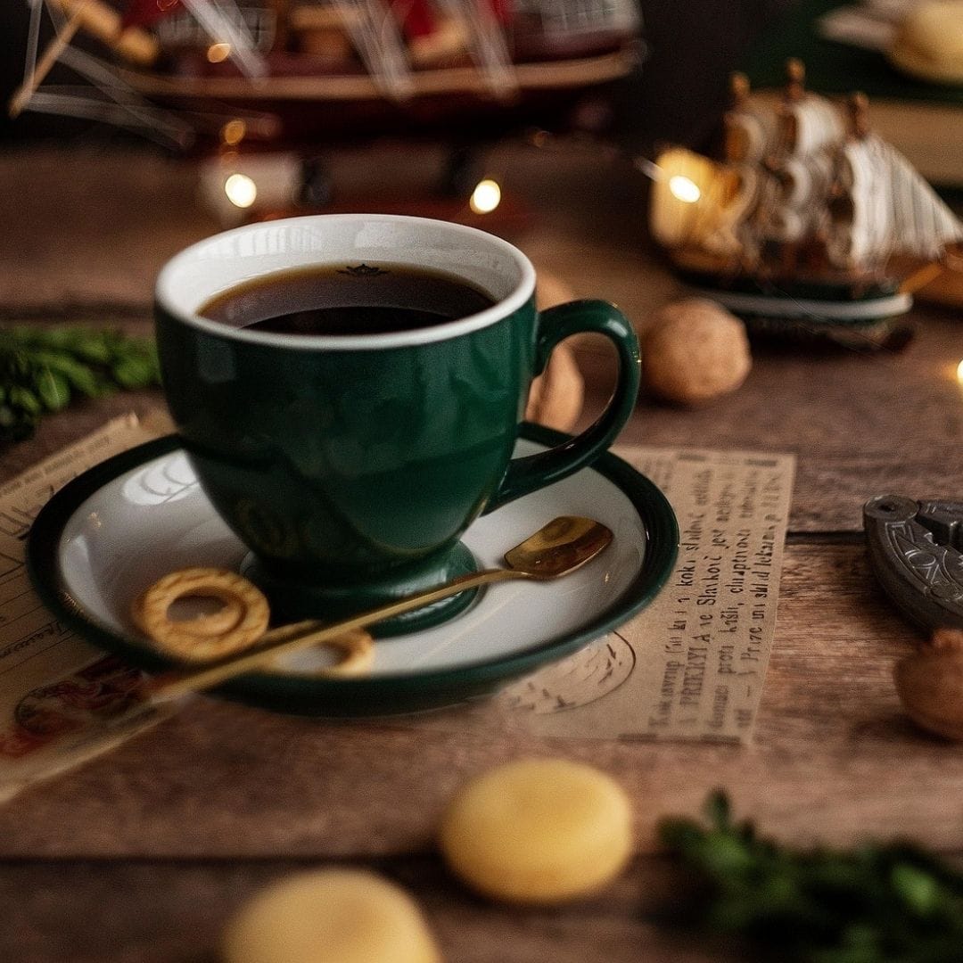 green coffee mug with macarons on an inviting table with golden lights in the background