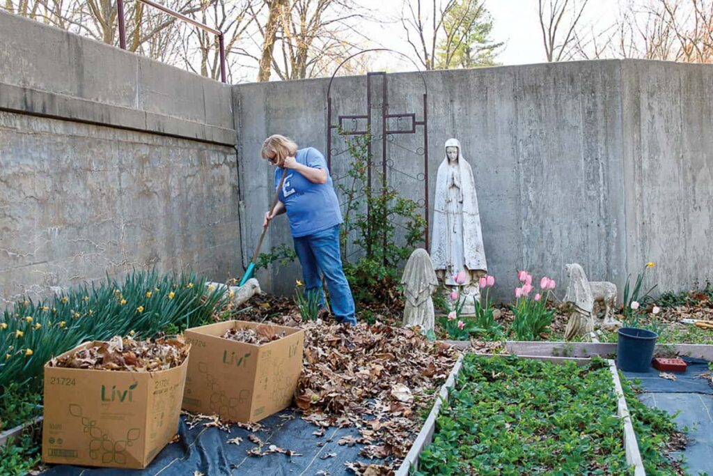 Oblate Janet Paper rakes in the garden.