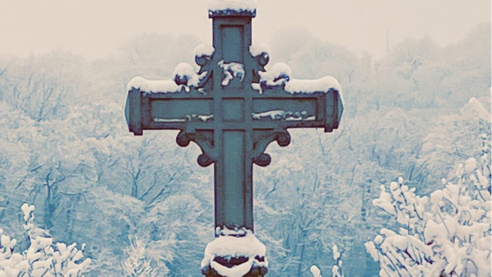 cross on mount st. scholastica campus with snow cover trees behind