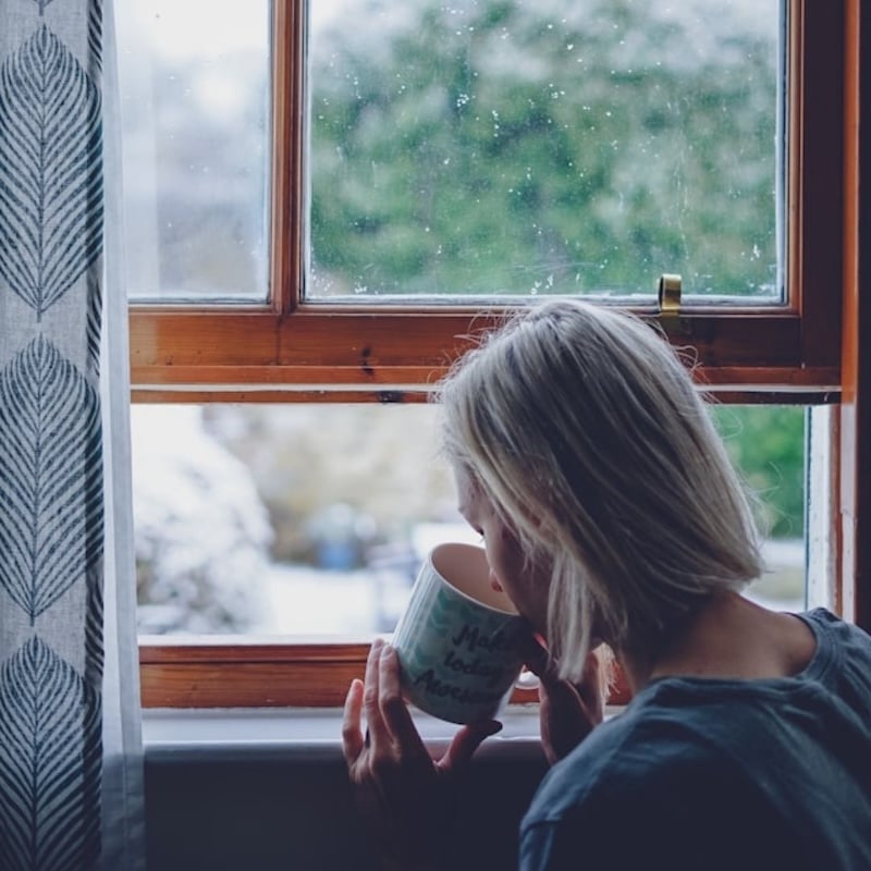 woman looking out window sipping on tea